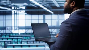 African american admin in data center running error checking utilities on tablet to fix hardware bugs. IT expert in server hub workspace looking for issues affecting mainframes performance, camera A video
