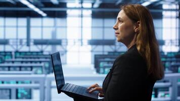 System administrator in server hub checking recovery plan on laptop, monitoring energy consumption. IT expert uses notebook in data center workspace, ensuring rigs are functioning optimally, camera A video