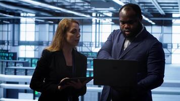 Team of IT specialists managing data center with advanced technology using devices. Coworkers in server room optimizing data center hardware equipment with laptop and tablet, camera A video
