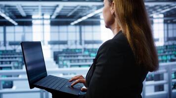 Technician doing checkup, inputting data on laptop of needed server hub fixes. Close up of employee working in data center housing advanced storage infrastructure supporting IT workloads, camera B video