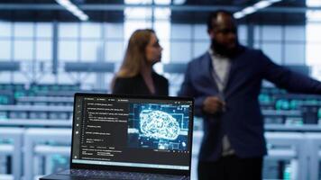 Close up of laptop with AI technology used to sustain data center hardware. Focus on notebook used by server room programmers in background using artificial intelligence tech, camera A video