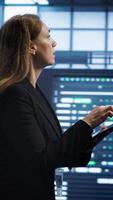 Vertical Technician doing checkup using tablet to prolong data center electronics life span and avoid downtime. Employee walking in server room, monitoring server infrastructure using digital device, camera A video