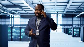 IT technician talking on phone in data center, coordinating server maintenance and troubleshooting tasks. Manager surrounded by server racks and high tech equipment in telephone call, camera A video