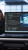 Vertical Focus on laptop in data center with artificial intelligence brain used by engineers in blurry background. Close up of device displaying AI deep learning software in server farm, camera A video