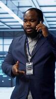 Vertical IT technician talking on phone in data center, coordinating server maintenance and troubleshooting tasks. Manager surrounded by server racks and high tech equipment in telephone call, camera A video
