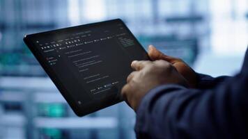Programmer monitoring server room rigs, doing checkup, inputting data on tablet of needed fixes. IT specialist working in data center facility housing storage hardware, camera A close up video