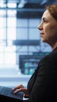 Vertical System administrator in server hub checking recovery plan on laptop, monitoring energy consumption. IT expert uses notebook in data center workspace, ensuring rigs are functioning optimally, camera A video