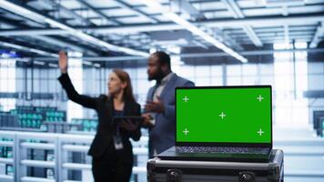 Green screen laptop used by engineers monitoring server room, doing checkup. Focus on chroma key notebook used by IT support employee working in data center facility, camera B close up video