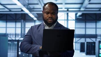 Computer scientist in data center using diagnostic tools and system monitoring software on laptop to identify cause of errors. IT specialist in server farm establishment repairing equipment, camera A video