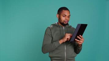 otimista homem adicionando Forma de pagamento método em conectados local na rede Internet usando tábua. pessoa emocionados para Faz Internet compras usando dispositivo, digitando débito cartão dados, isolado sobre estúdio fundo, Câmera b video