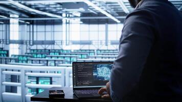 Software developer in data center using artificial intelligence computing simulating human brain. IT support staff member working on notebook with AI machine learning algorithms, camera B video