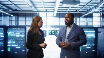 African american expert and coworker looking at holograms in data center, working together. Team members interacting with augmented reality AI visualization in server hub, camera B video