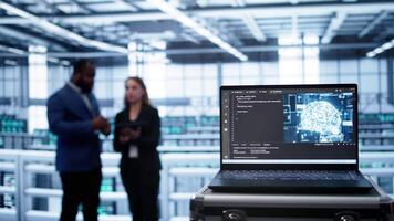 Focus on laptop in data center with artificial intelligence brain used by engineers in blurry background. Close up of device displaying AI deep learning software in server farm, camera B video