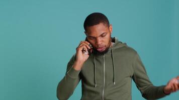 Irked african american man fighting with friends during telephone call, isolated over studio background. Outraged person arguing with mates during conversation on mobile phone, camera A video
