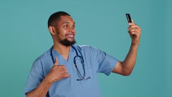 Male nurse using mobile phone to take selfies during hospital job shift break. Healthcare worker using smartphone to take pictures of himself, isolated over studio background, camera A video