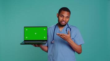 Portrait of practitioner in medical uniform showing instructions on isolated screen laptop. Healthcare professional doing presentation using mockup notebook, studio backdrop, camera B video