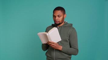 Man laughing while reading funny book, entertained by engrossing story. Joyful person having fun, being amused by literature novel during leisure time in studio background, camera B video