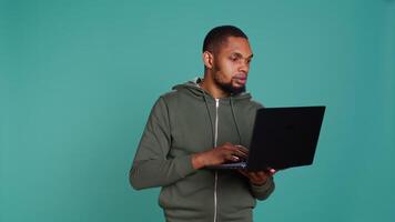 Man typing on laptop keyboard, checking emails, feeling overjoyed after receiving good news. Employee sending mail online, celebrating after meeting KPIs at work, studio background, camera B video