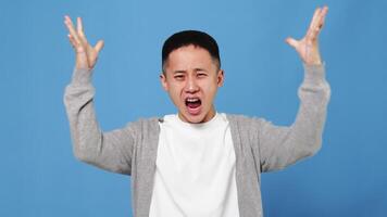 Portrait of a young asian man feeling upset and shocked, touching her head and showing a mind explosion gesture on a blue background in the studio video