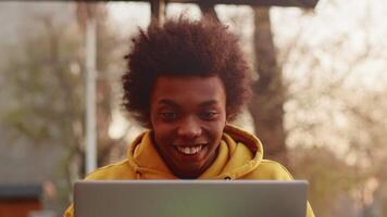 Young black programmer in casual clothes sitting outdoors with a laptop and becoming overjoyed due to unexpected success in working issues close up video
