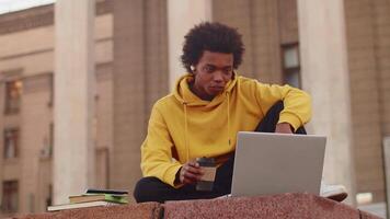 Young black programmer in casual clothes talking with a client on a call on a laptop while sitting outdoors near the building. Concept of flexible remote work video