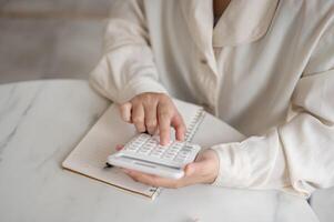 A close-up image of a woman using a calculator at a table, checking and calculating her budget. photo