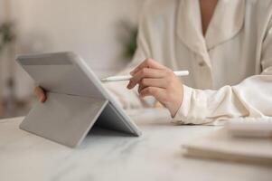 A woman holding a stylus pen and using her digital tablet, working remotely from a cafe. photo