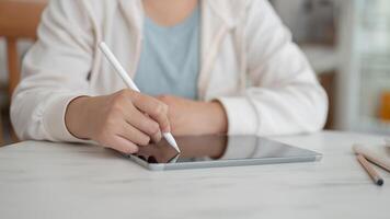 A cropped image of a student working remotely from a cafe, writing on a tablet with a stylus pen. photo