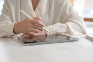 A woman working remotely from a cafe, holding a stylus pen and working on her digital tablet. photo