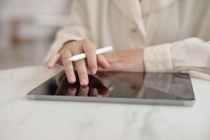 A woman working remotely from a cafe, holding a stylus pen and working on her digital tablet. photo