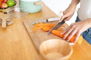 A close-up image of a woman cutting a carrot on a cutting board, cooking in the kitchen. photo