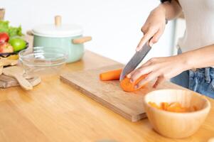 A close-up image of a woman cutting a carrot on a cutting board, cooking in the kitchen. photo