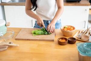 A close-up image of a woman cutting lettuces on a cutting board, cooking in the kitchen. photo