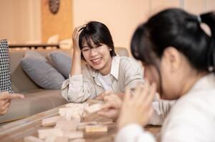 A cheerful Asian woman is laughing and enjoying playing a tabletop game with her friends at home. photo