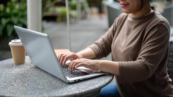 un recortado imagen de un asiático mujer trabajando en su ordenador portátil computadora, trabajando remotamente al aire libre. foto
