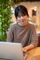A young attractive Asian woman working remotely from a coffee shop, working on her laptop computer. photo
