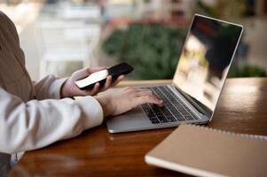 A woman in hoodie using her laptop computer at a table in a coffee shop, working remotely. photo