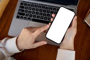 Top view image of a woman using her smartphone at her working desk. A white-screen smartphone mockup photo