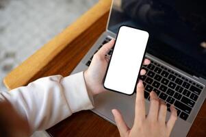 Top view image of a woman using her smartphone at her working desk. A white-screen smartphone mockup photo