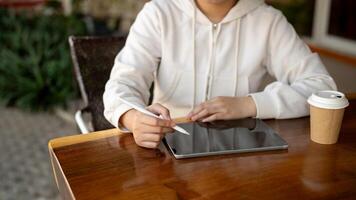 Cropped image of a woman in a hoodie is using her digital tablet at a table in a coffee shop. photo