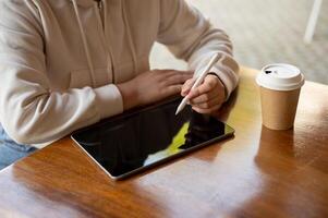 Cropped image of a woman in a hoodie is using her digital tablet at a table in a coffee shop. photo