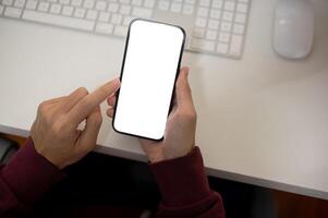 Top view image of a man using his smartphone at her office desk. A white-screen smartphone mockup photo