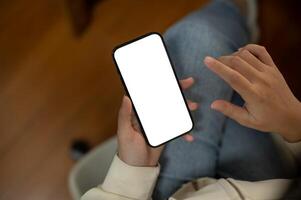 Top view of a woman is using her smartphone while sitting indoors. A white-screen smartphone mockup photo