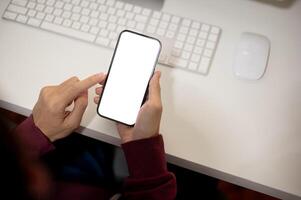 Top view image of a man using his smartphone at her office desk. A white-screen smartphone mockup photo