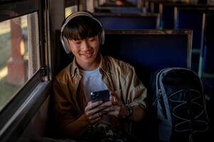 A happy Asian man is using his phone and listening to music while he is on a train to somewhere. photo