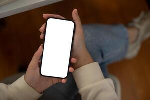Top view of a woman is using her smartphone while sitting indoors. A white-screen smartphone mockup photo