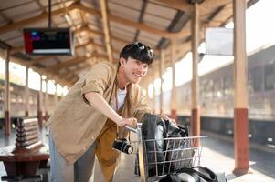 An excited Asian man traveler is walking down the platform with a cart, waiting for his train. photo