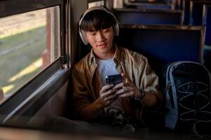 A happy Asian male is listening to music and using his phone while commuting by train to somewhere. photo