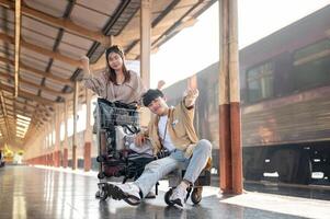 Cheerful couple are walking down the platform with a cart, commuting by a train at a railway station photo