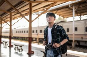 A handsome, happy young Asian man tourist backpacker standing at a platform in a railway station. photo